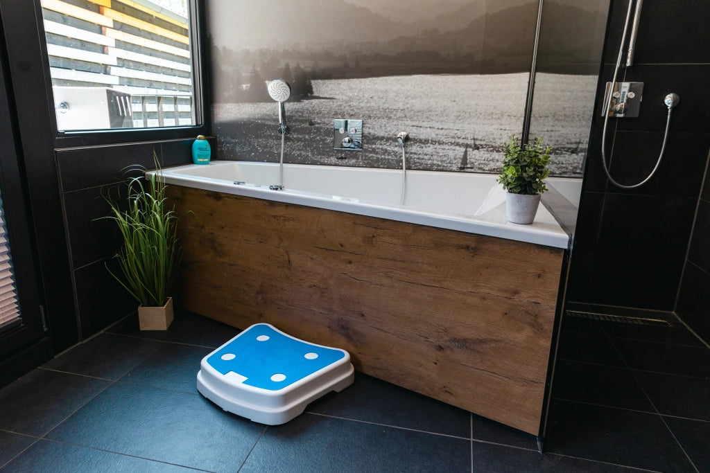 Badewannentritt Sky von Drive Medical vor einer Badewanne in modernem Badezimmer – rutschfeste Einstiegshilfe mit blauer Trittfläche für sicheres Ein- und Aussteigen.
